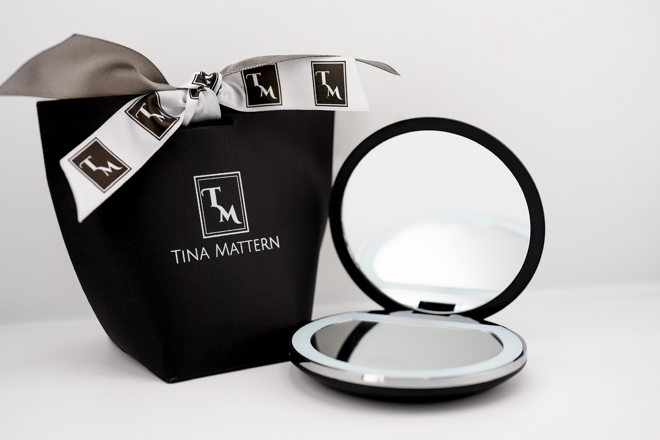 Black Tina Mattern gift bag with white ribbon and an open LED compact mirror