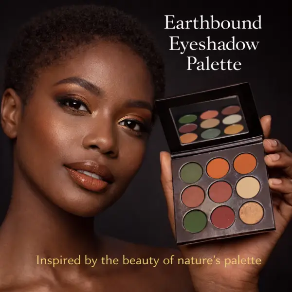 Black female model wearing Earthbound Eyeshadow Palette with olive green, burnt orange, and brown eyeshadow look, holding open palette against dark background
